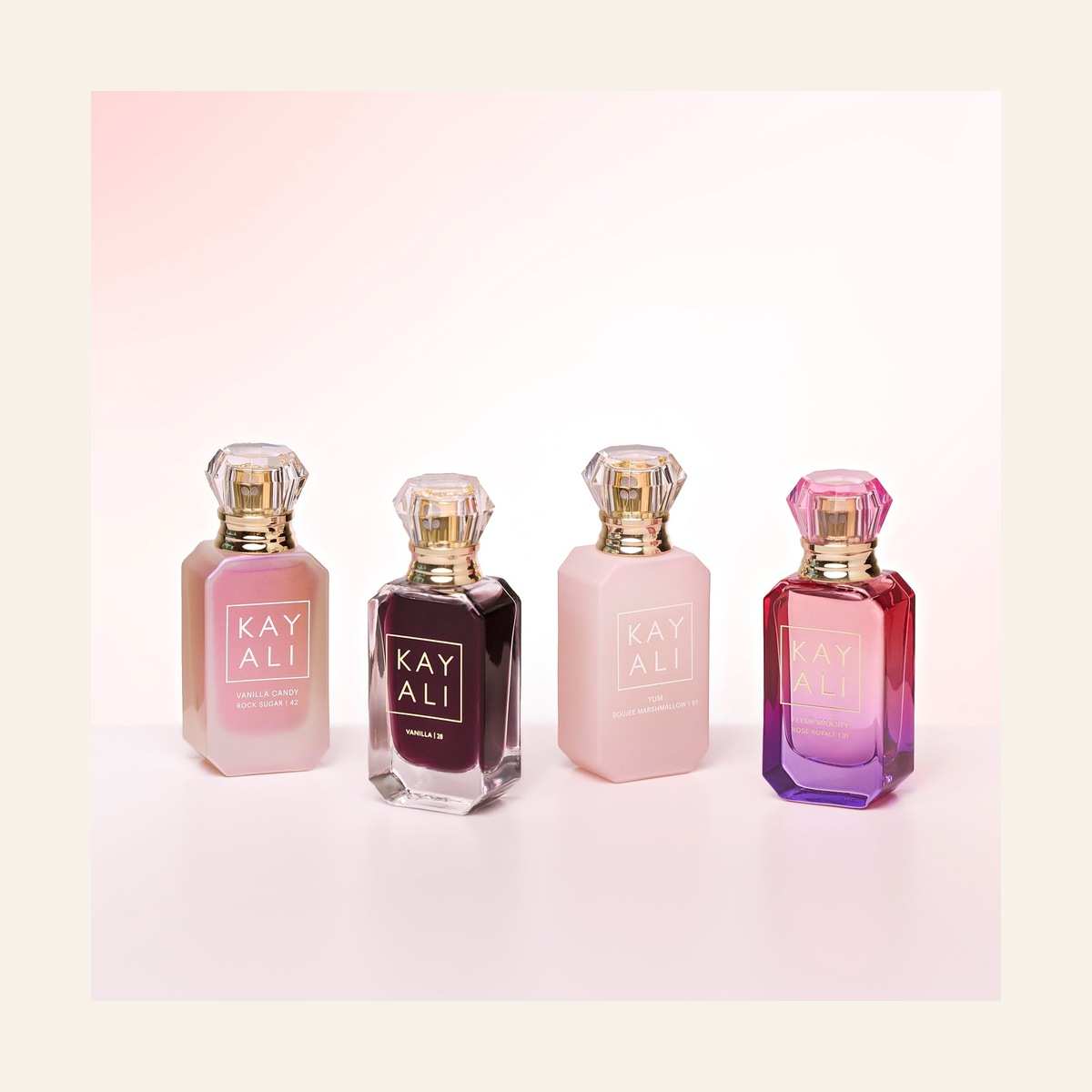KAYALI Sweet Obsessions four miniature fragrance bottles arranged on a pink background