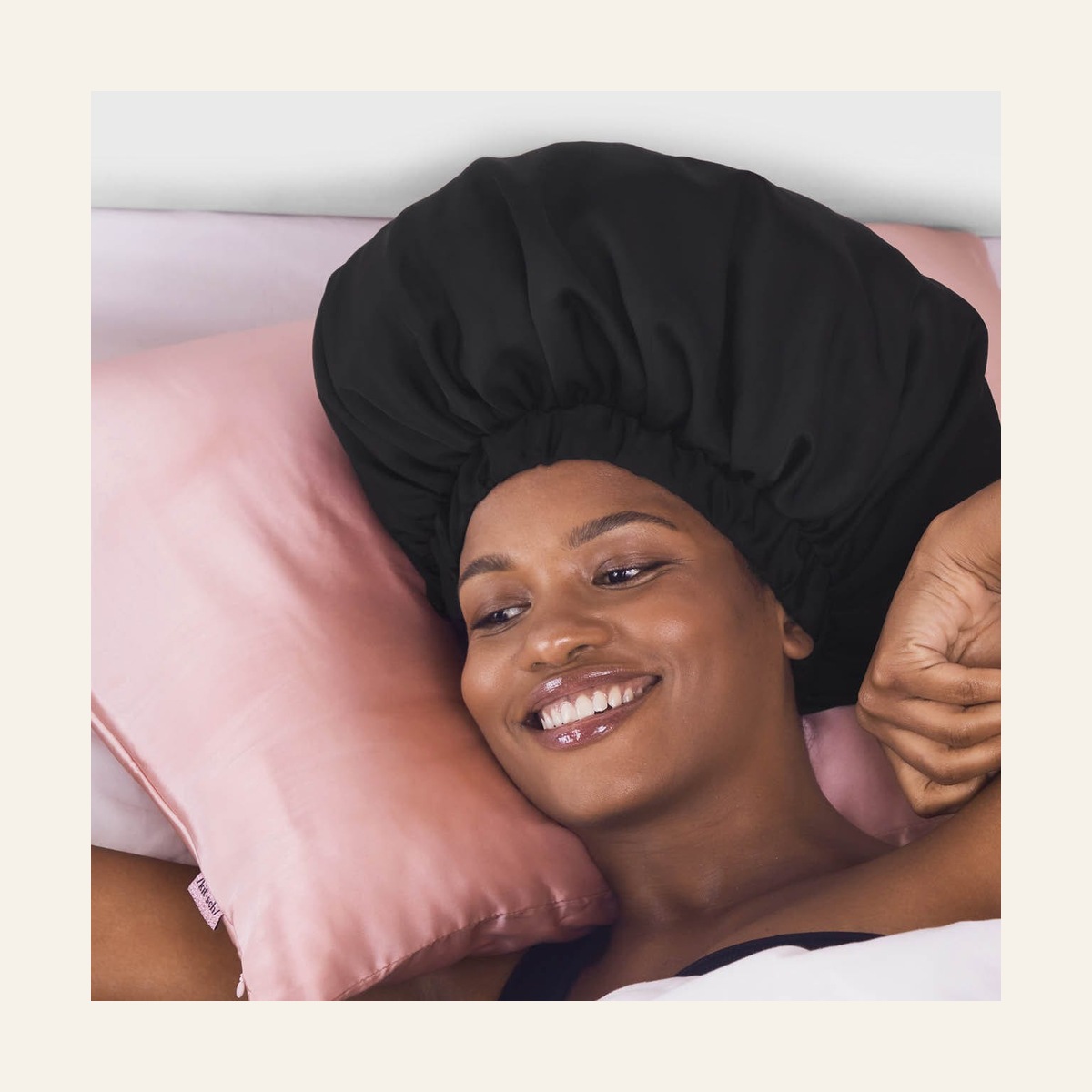 Model resting on a pillow while wearing the black Kitsch XL satin bonnet