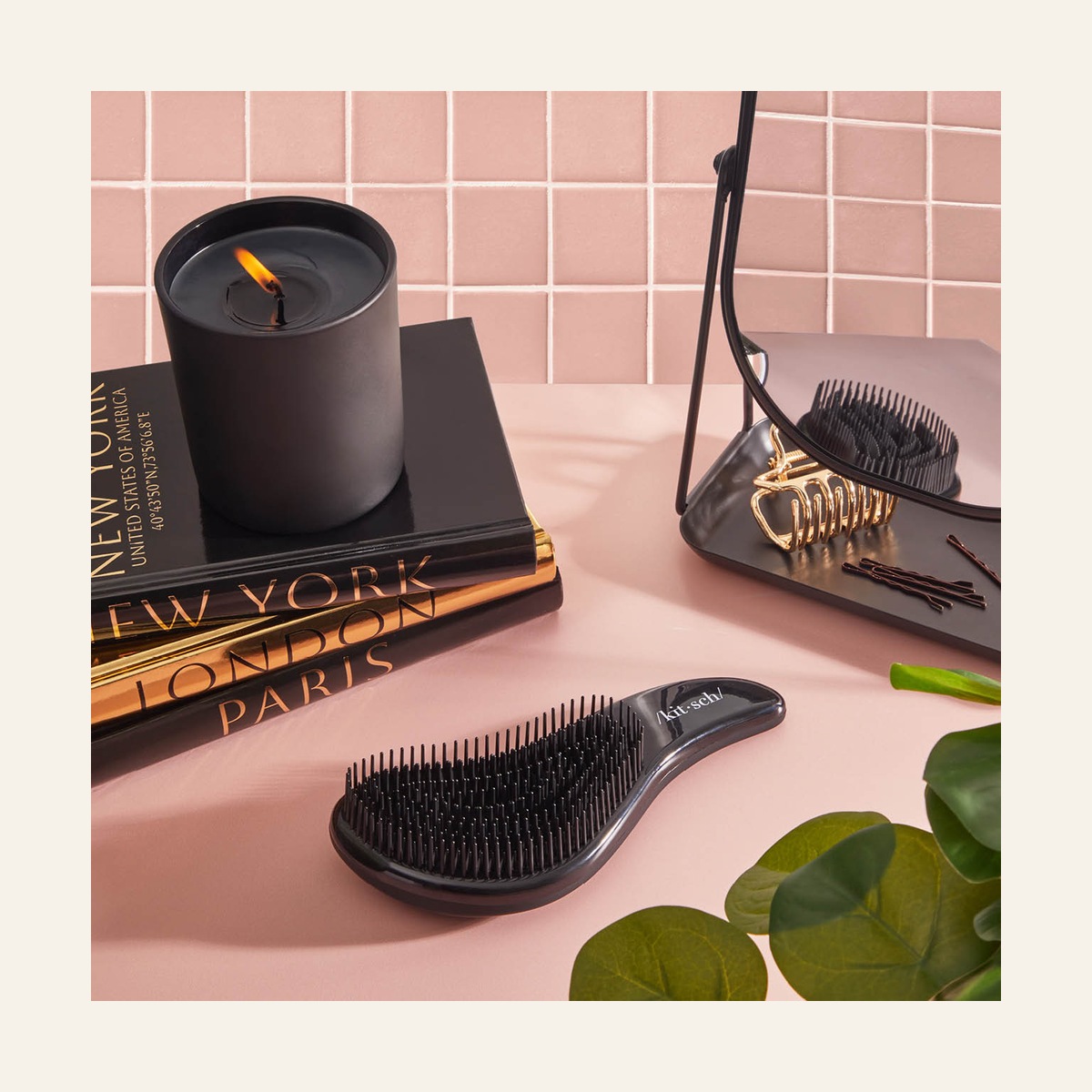 Black Kitsch detangling brush on a pink vanity beside other hair accessories