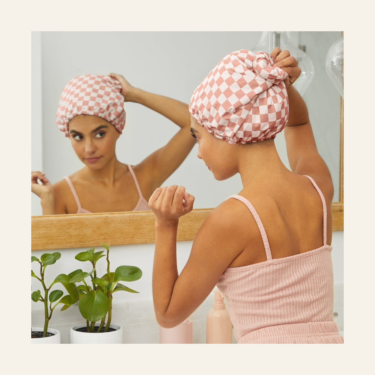 Rear view of a model adjusting the Terracotta Checker shower cap in a mirror