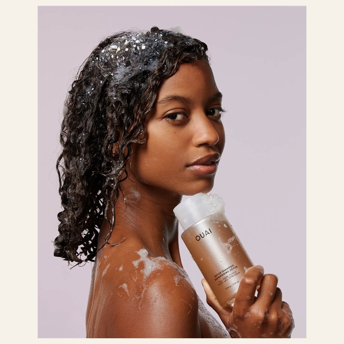 Model holding OUAI Detox Shampoo with lather in her hair